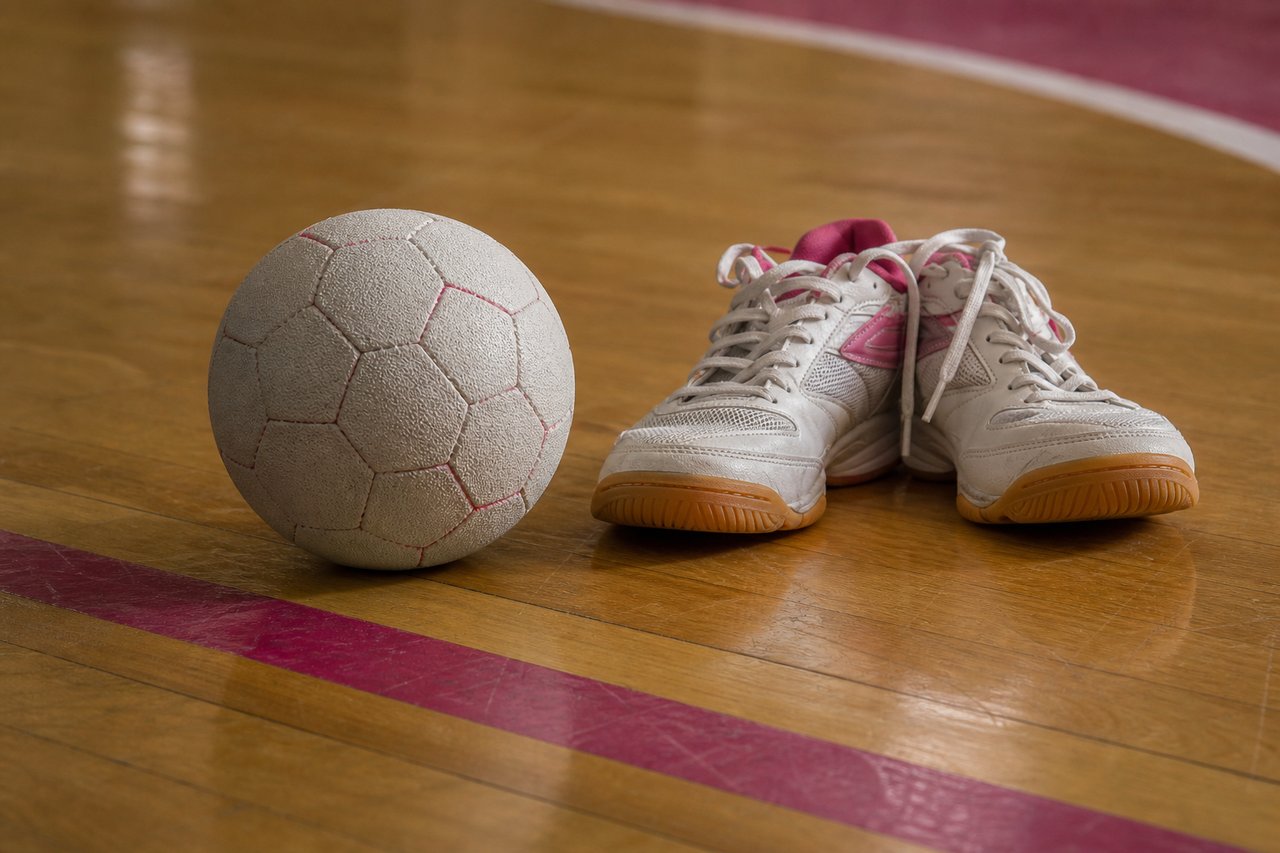 Hallenboden mit aufgemalten Linien, davor ein Handball und ein Paar Hallenschuhe